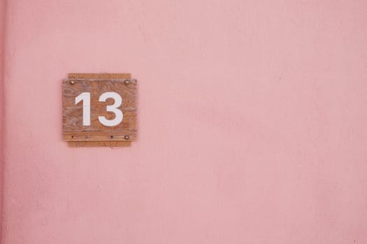House number thirteen displayed on a pink wall under bright sunlight.