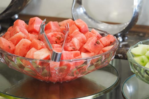 Colorful watermelon cubes are arranged in a crystal bowl at a gathering.