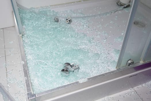 Broken glass lays across the floor of a shower enclosure after an accident.