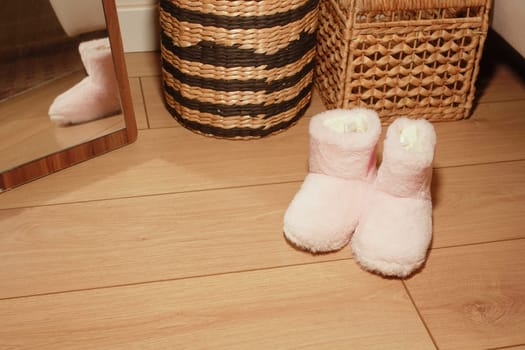 Soft pink slippers resting on wooden floor next to woven storage baskets.