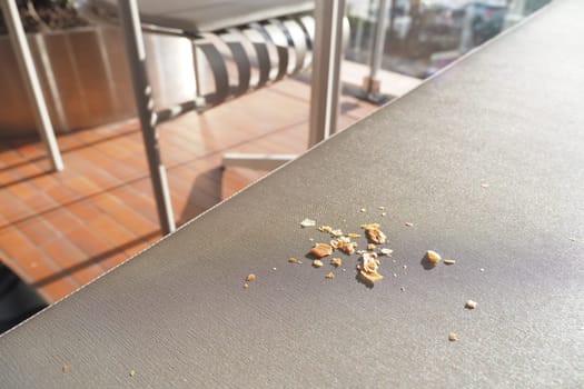 Small pieces of food litter a sunlit outdoor table setting.