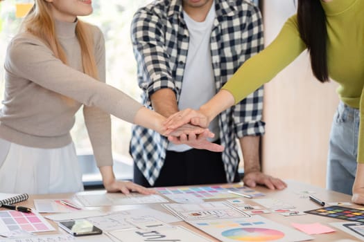 Diverse team members celebrating collaboration and success by placing their hands together over a table filled