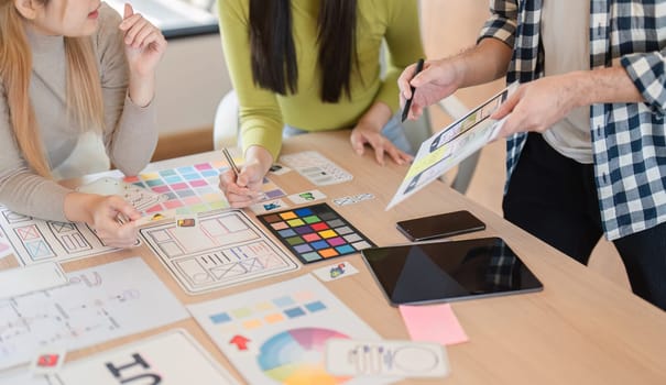 A close-up view of a diverse team collaborating over design materials, analyzing colors, and discussing concepts at a table in a modern office.