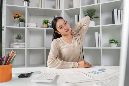 A woman stretching her neck to relieve discomfort while working at her desk, illustrating the effects of office syndrome in a professional setting.