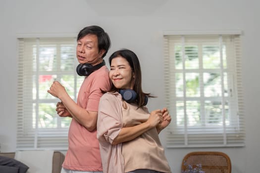 A joyful diverse couple dances back to back, enjoying music with headphones in their comfortable home setting.