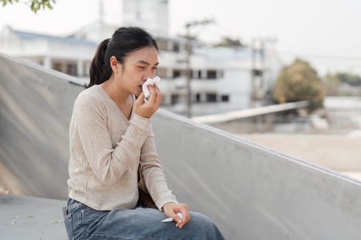 A diverse woman wearing a mask, wiping her tears while sitting outdoors in a city setting, displaying vulnerability.
