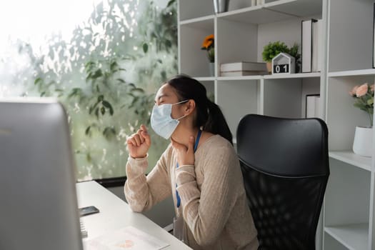 A woman wearing a mask, feeling discomfort while working at her desk, highlighting health challenges in a modern office environment.