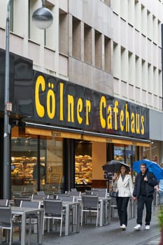 Cologne, Germany – May 24, 2024: Cologne city center with walkers in front of a café in rainy weather