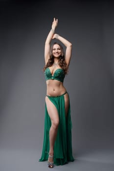 A skilled belly dancer showcases her talent, dressed in a stunning green costume, while posing gracefully in a studio environment.