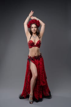 A graceful dancer showcases her skills in a stunning red outfit adorned with flowers, performing artfully against a neutral backdrop.