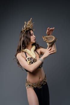 A dancer adorned in shimmering attire interacts gracefully with a snake, highlighting an artistic performance in a well-lit studio.