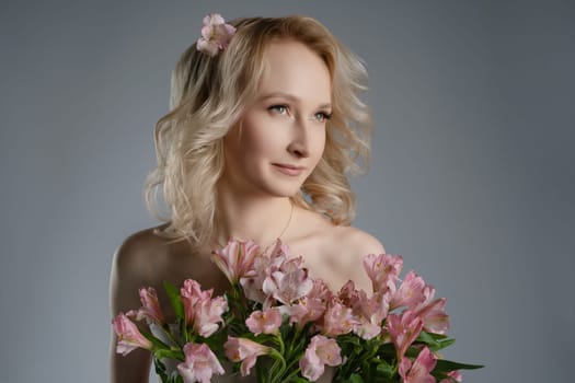 A female model stands elegantly in a studio, holding a vibrant bouquet of flowers and wearing a soft expression, surrounded by a neutral background.