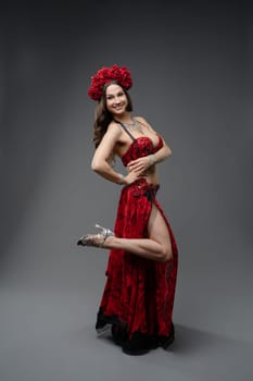 A dancer showcases her vibrant red outfit adorned with roses, striking a graceful pose in a studio setting, emphasizing her artistic expression.