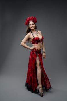 A vibrant dancer showcases her traditional red costume with a floral headpiece, standing confidently in front of a neutral background.