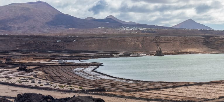 Coastal salt flats with mountains under a cloudy sky highlight nature's harmony and industrial contrast.