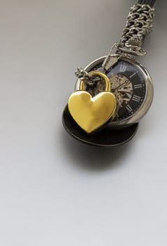 Golden heart shaped love padlock lap over A retro pocket watch on white background. Love can endure beyond the limitations of time, Concept of Love that transcends time, Valentine's day, use it as your Copy space, Design, Wallpaper and Poster, Selective focus.