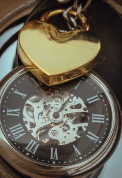 Close-up of Golden heart shaped love padlock lap over A retro pocket watch. Love can endure beyond the limitations of time, Concept of Love that transcends time, Valentine's day, use it as your Copy space, Design, Wallpaper and Poster, Selective focus.