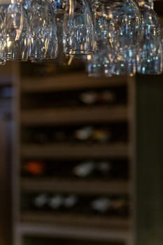 Clean wine glasses hanging over the bar counter on out of focus background with shelf with bottles of wine