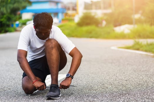 Close up Asian sport runner black man wear watch sitting he trying shoelace running shoes getting ready for jogging and run outdoor street health park with copy space, healthy exercise workout concept