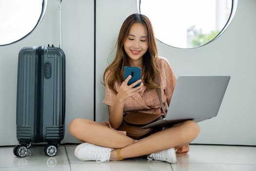 Woman sitting comfortably on the floor with her suitcase and smartphone, enjoying her vacation at the airport. Tourist journey trip concept