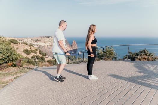 Happy Middle aged couple or friends practicing nordic walking in park near sea. Mature couple with trekking poles walking, practicing Nordic walking outdoors. Aging youthfully and sport concept.