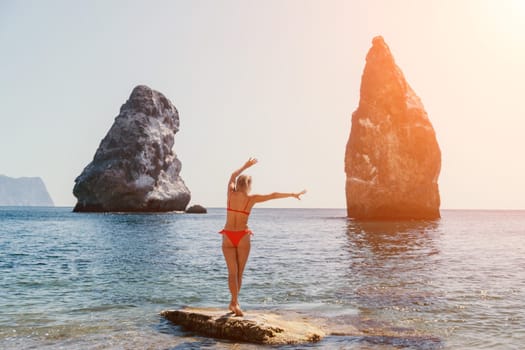 Woman travel sea. Young Happy woman in a long red dress posing on a beach near the sea on background of volcanic rocks, like in Iceland, sharing travel adventure journey