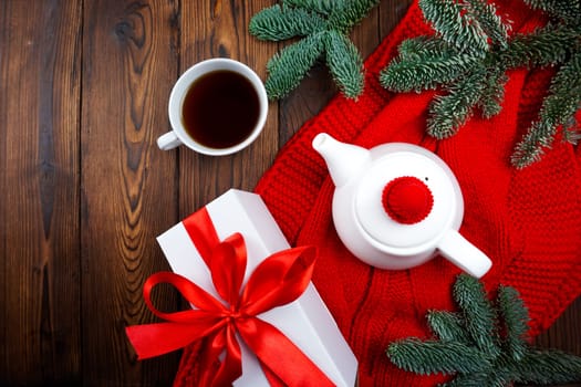 On a wooden background there is a red scarf and there is a teapot and a cup of tea. High quality photo