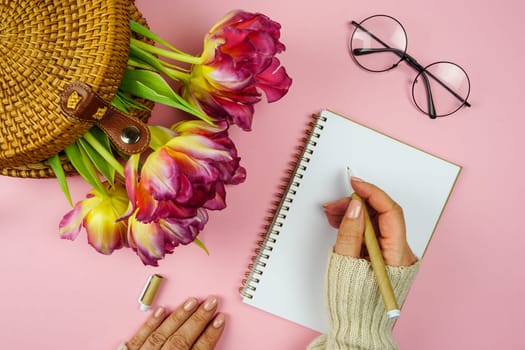 A woman's hand writes down plans in a notebook, there are tulips in a wicker bag on the table. High quality photo