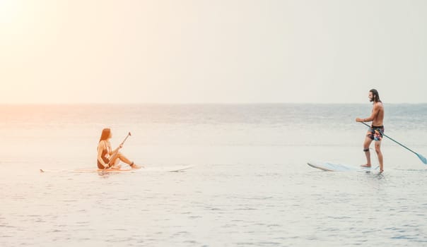Sea woman and man on sup. Silhouette of happy young woman and man, surfing on SUP board, confident paddling through water surface. Idyllic sunset. Active lifestyle at sea or river