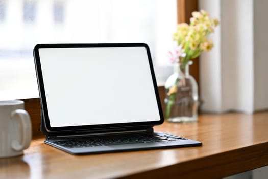 Wooden office desk with digital tablet, pencil holder and coffee cup. Blank screen for your advertising text message.