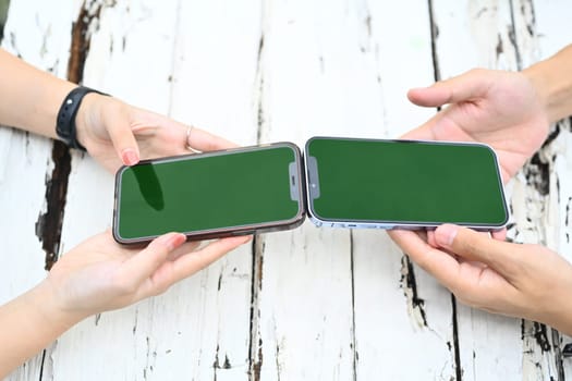 Unrecognizable young people bringing the top half of two smartphones closer for sharing files or contacts between devices.