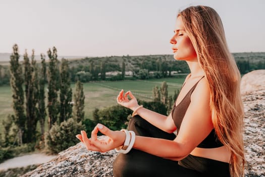 Well looking middle aged woman with long hair, fitness instructor in leggings and tops doing stretching and pilates on the rock near forest. Female fitness yoga routine concept. Healthy lifestyle.