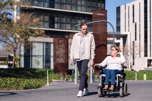 woman using electric wheelchair with a young man talking happy as they walk through the city, concept of friendship and diversity, copy space for text