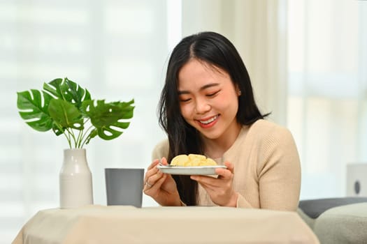 Cheerful young asian woman in casual clothes having breakfast at home. Concept of wellness, food and domestic lifestyle.
