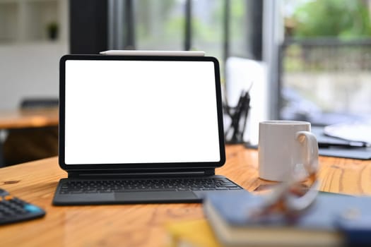 Wooden office desk with digital tablet, pencil holder and coffee cup. Blank screen for your advertising text message.