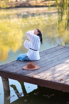 Autumn lake woman. She sits by a pond on a wooden pier in autumn and admires nature. The concept of tourism, weekends outside the city