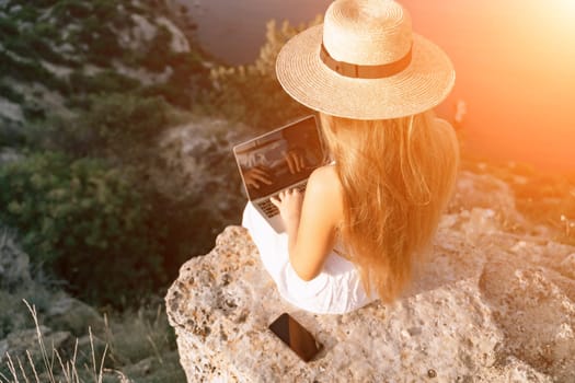 Freelance happy woman typing on her laptop, enjoying the picturesque sea view, highlighting the idea of working remotely with a relaxed and pleasant atmosphere