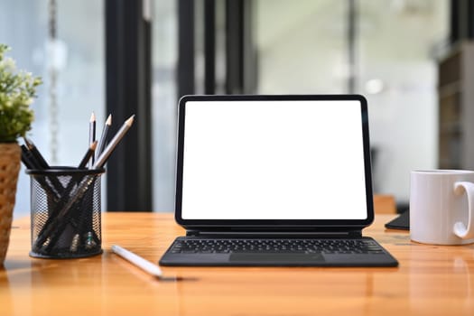 Wooden office desk with digital tablet, pencil holder and coffee cup. White screen for your advertising text message.