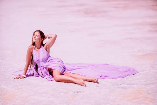 A woman in a pink dress sits on the salty shore of a pink lake and poses for a souvenir photo, creating lasting memories