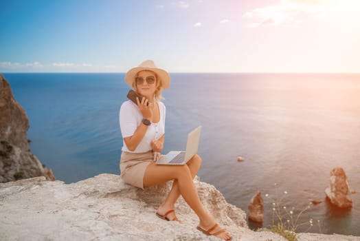 Freelance women sea working on the computer. Good looking middle aged woman typing on a laptop keyboard outdoors with a beautiful sea view. The concept of remote work