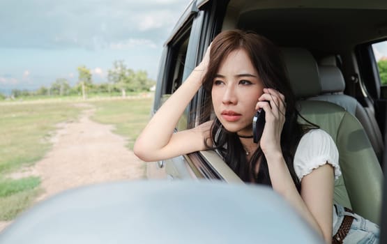 Stressed and confused Asian woman calls insurance on faulty car while traveling together.