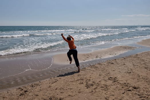 Boy jumping over puddle of water on the beach.Caucasian, brown hair, barefoot, sandy beach, water with waves,