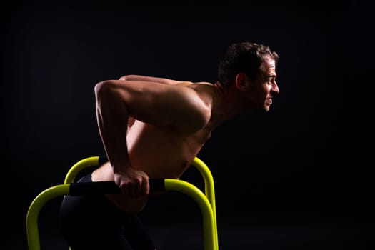 Front and side view photo of strong young man exercising on parallel bars in studio.