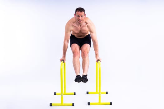 Front and side view photo of strong young man exercising on parallel bars in studio.