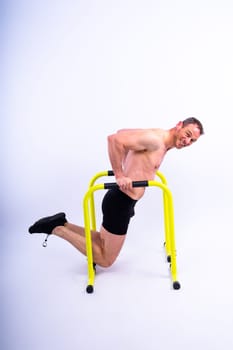 Front and side view photo of strong young man exercising on parallel bars in studio.