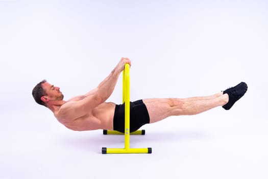 Front and side view photo of strong young man exercising on parallel bars in studio.