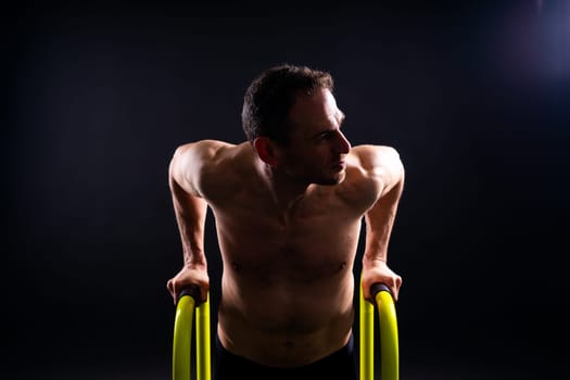 Front and side view photo of strong young man exercising on parallel bars in studio.