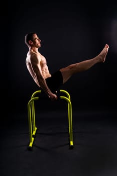 Front and side view photo of strong young man exercising on parallel bars in studio.