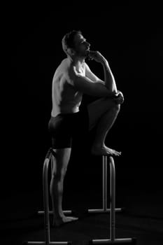 Front and side view photo of strong young man exercising on parallel bars in studio.