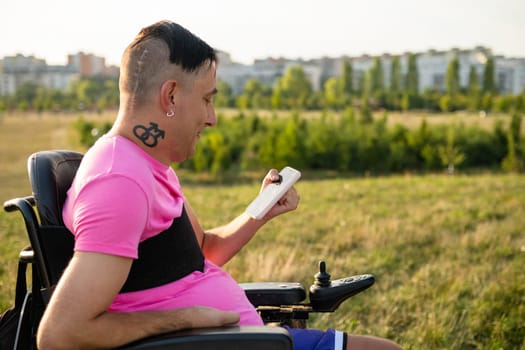 LGBT person with a disability in a wheelchair, actively using a mobile phone for online work in the park